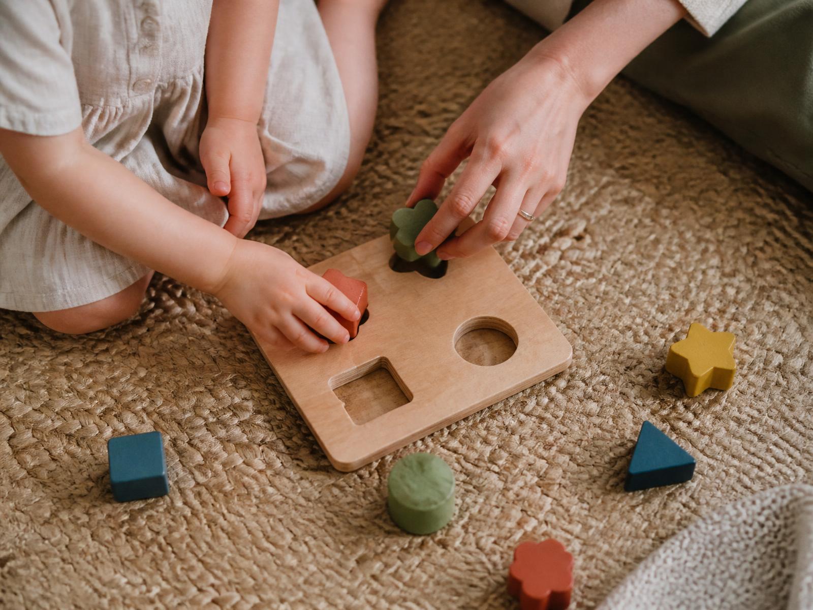 Child and therapist collaborating with a wooden shape-sorter toy during an in-home ABA session